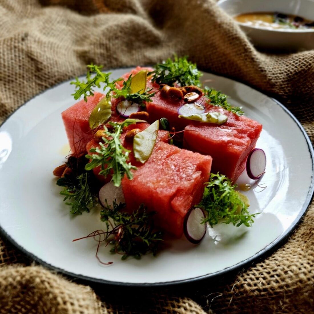 image of watermelon salad plated with garnish on burlap background