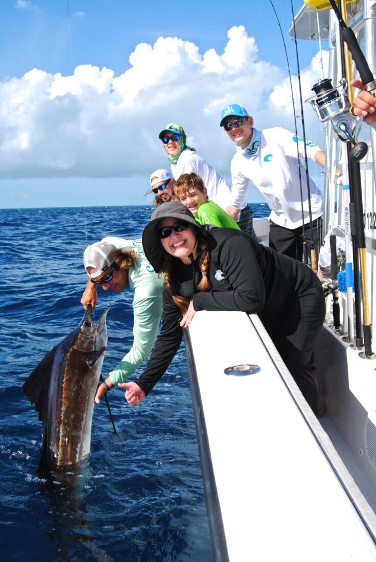People reel in a sailfish on a boat