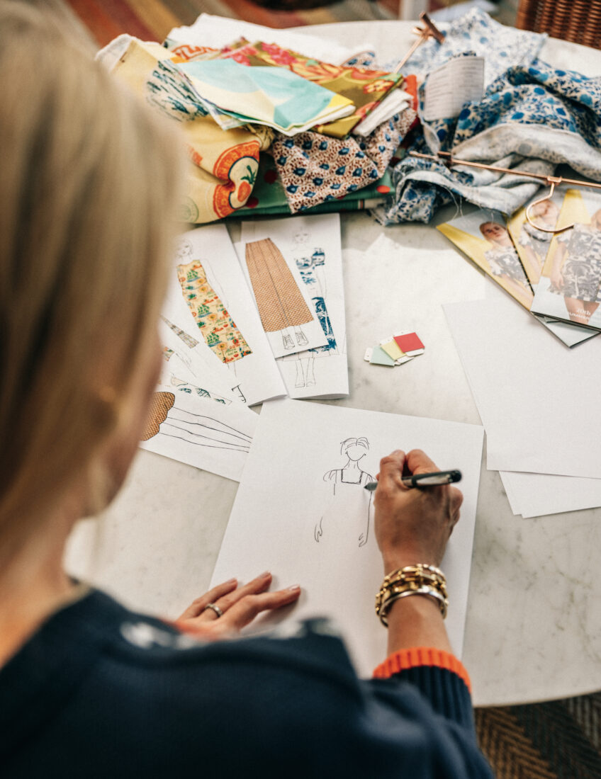 A woman sketches clothing designs at a table