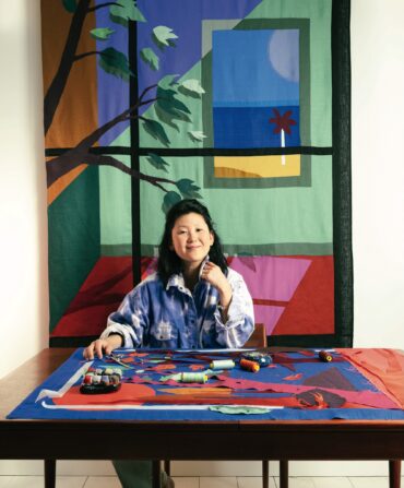 A woman in an art studio with fabric and a fabric artwork of a window behind her