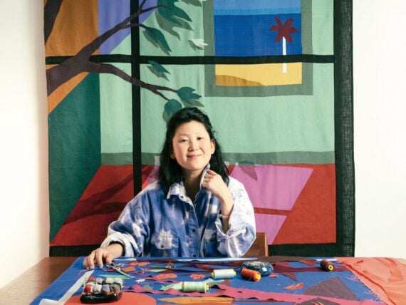 A woman in an art studio with fabric and a fabric artwork of a window behind her