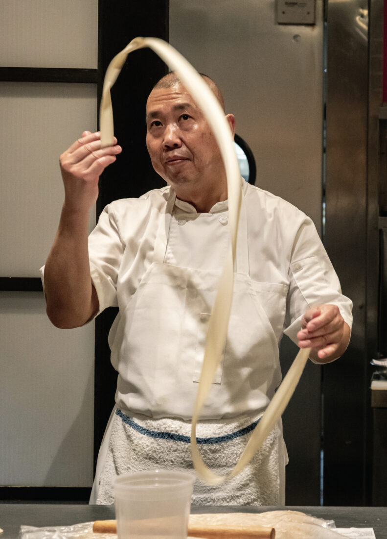 A man makes hand-pulled wide noodles.