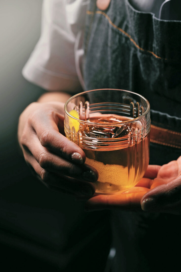 A glass of bourbon in someone's hand