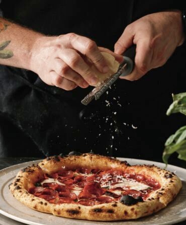 A person grates cheese onto a pizza