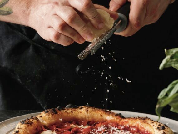 A person grates cheese onto a pizza