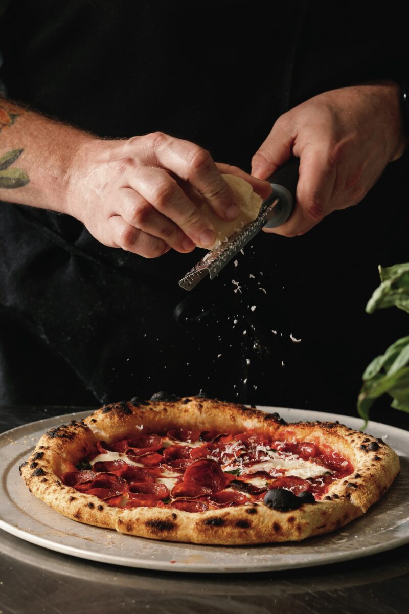 A person grates cheese onto a pizza