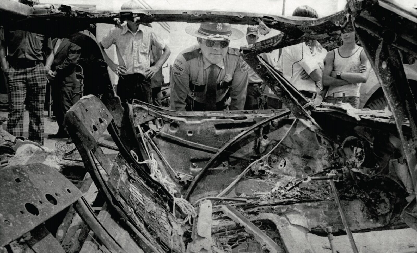 A black and white image of a cop looking at a car wreck