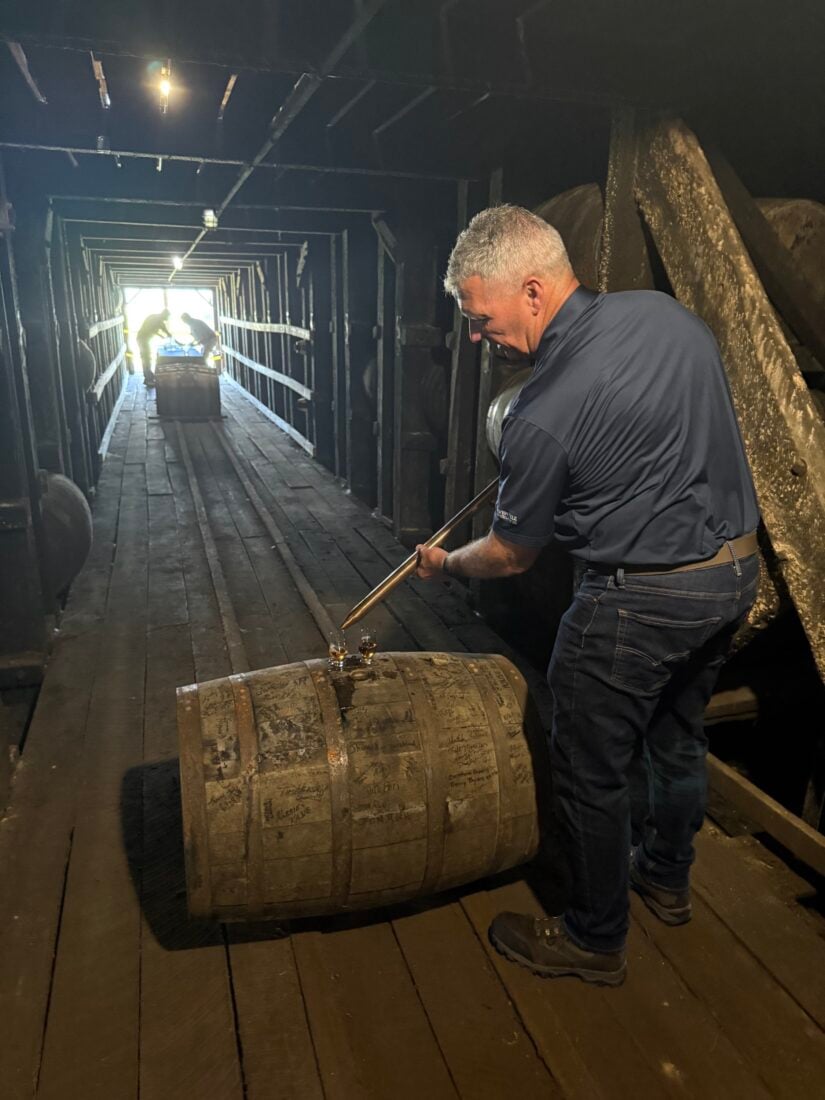 A man samples bourbon from a barrel