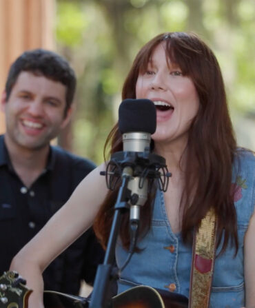 A singer at a microphone with band members nearby