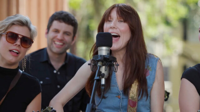 A singer at a microphone with band members nearby