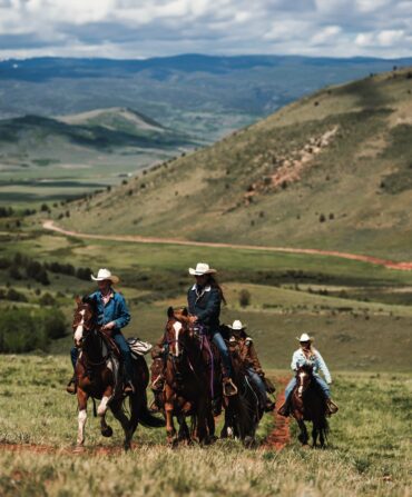 People ride horses against a mountain landscape