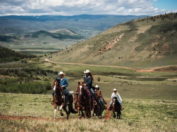 People ride horses against a mountain landscape