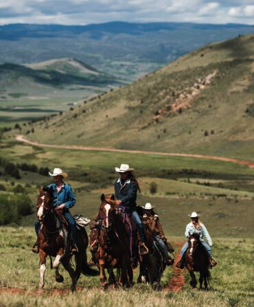 People ride horses against a mountain landscape