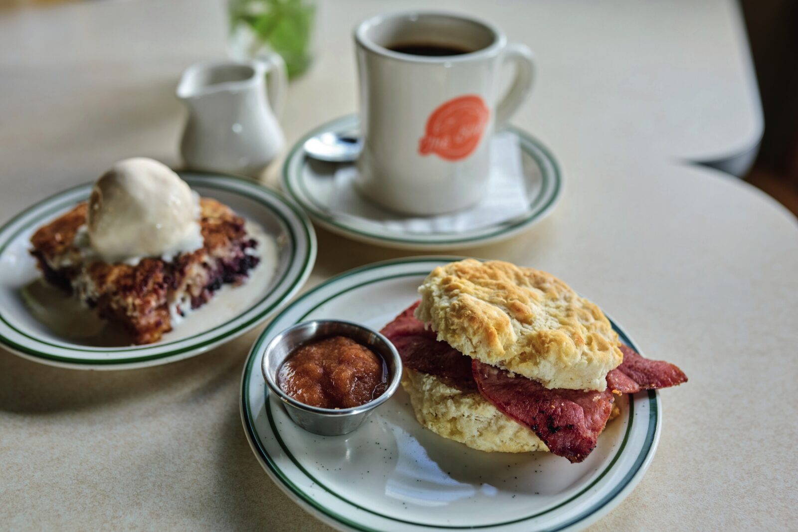 A country ham biscuit and pie slice on a table with a mug of coffee